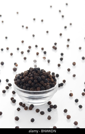 Pepe nero in granelli in piccola ciotola di vetro con pepe diffusa Foto Stock