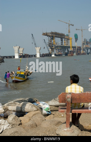 Ragazzo che guarda a faticando pescatori con mare link (fase di costruzione) in background - Worli - Koliwada, Mumbai, India Foto Stock