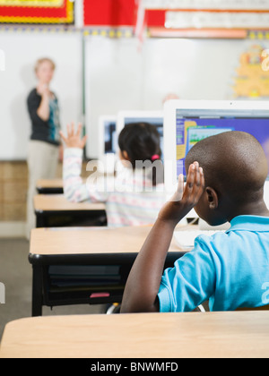 Gli studenti della scuola elementare ad alzare la mano in classe Foto Stock