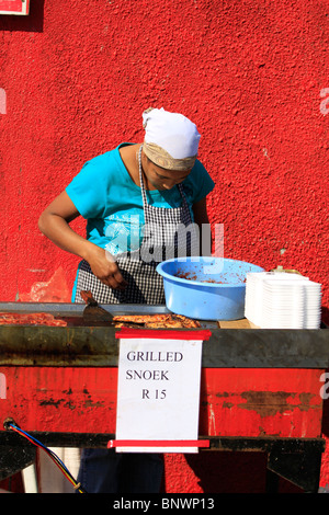 Donna locale la cottura alla griglia appena catturati snoek a Hout Bay Harbor vicino a cape town, Sud Africa. Foto Stock