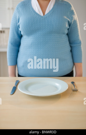 Il sovrappeso donna in piedi nella parte anteriore del posto impostazione Foto Stock