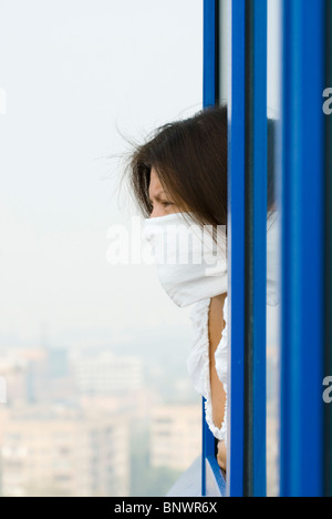 Muscovite donna in maschera protettiva guardando da una finestra Foto Stock