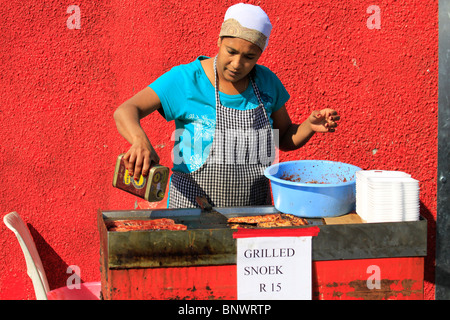 Donna locale la cottura alla griglia appena catturati snoek a Hout Bay Harbor. Foto Stock