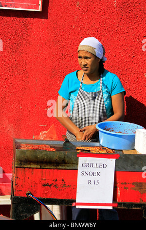 Donna locale la cottura alla griglia appena catturati snoek a Hout Bay Harbor. Foto Stock