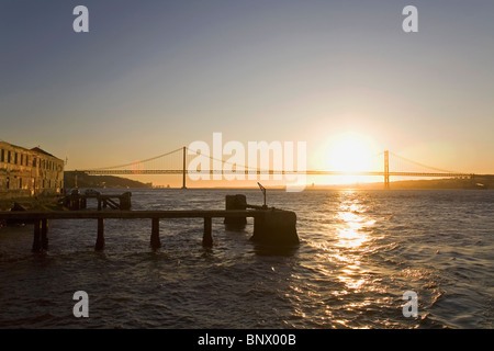 Il sole tramonta sul fiume Tago (Rio Tejo) nella parte anteriore del 25 aprile Bridge (Ponte de 25 Abril) a Lisbona, Portogallo. Foto Stock