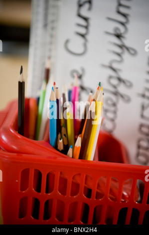 Matite colorate in rosso cesto in plastica con la scrittura di aids in una scuola primaria della classe. Foto Stock