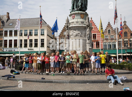 Belgio Europa il gruppo di scolari in Markt sul viaggio scolastico di cantare una canzone davanti a un monumento a eroi di Bruges mattutino Foto Stock