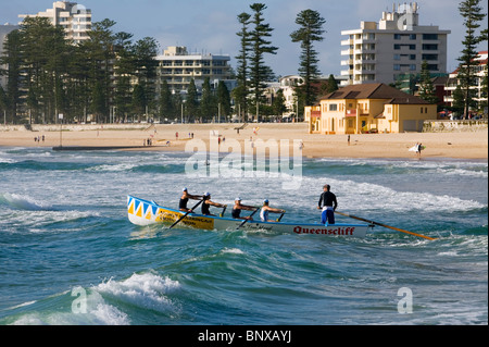 Un team surfboat righe nelle onde a Manly Beach Sydney, Nuovo Galles del Sud, Australia Foto Stock