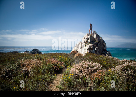 Una giovane donna sorge in cima a una roccia che si affacciano sull'Oceano Pacifico Foto Stock