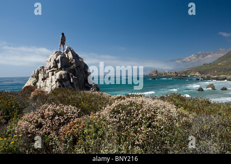 Una giovane donna sorge in cima a una roccia che si affacciano sull'Oceano Pacifico Foto Stock