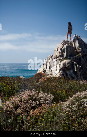 Una giovane donna sorge in cima a una roccia che si affacciano sull'Oceano Pacifico Foto Stock