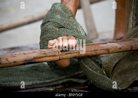 Fisherman's piede sul bordo della sua barca, avvolto in rete da pesca, nella cittadina di Chau Doc, Vietnam Foto Stock