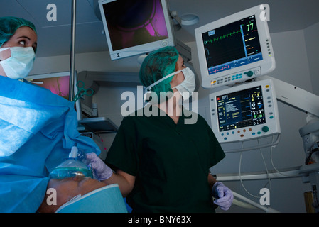 Anestesista medico di controllo attrezzature informatiche per monitorare le condizioni del paziente durante il funzionamento Foto Stock