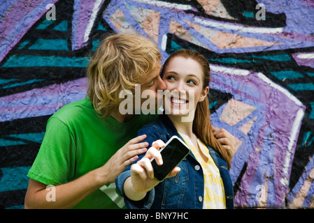 Coppia giovane fotografa se stessi con un telefono cellulare, maschio femmina baciando la guancia Foto Stock