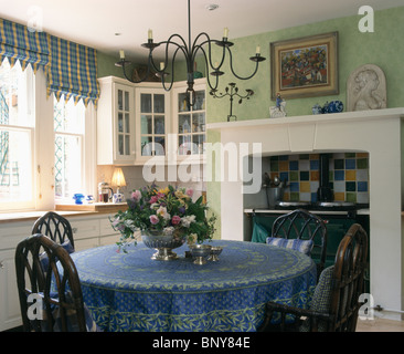 Lampadario in metallo al di sopra tavola circolare con panno blu nel verde pallido cucina con nero Aga e finestra con cieco controllato Foto Stock