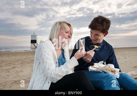 Coppia sulla spiaggia a mangiare pesce e patatine Foto Stock