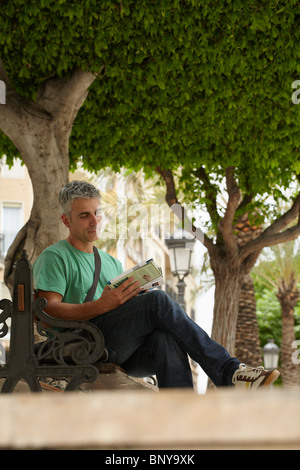 Uomo seduto sul banco la guida di lettura Foto Stock