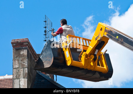 Antenna televisione essendo dotato di camino dall uomo in piedi (nessuna attrezzatura di sicurezza) in JCB movimentatore telescopico benna - Francia. Foto Stock