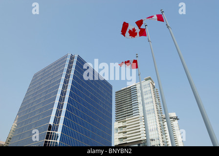 Torri di vetro riflettente edifici circostanti con tre bandiere canadesi in prua anteriore, nel centro cittadino di Vancouver Foto Stock