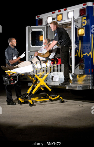 I paramedici la cura per il paziente anziano sulla barella in ambulanza a notte Foto Stock