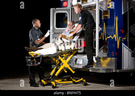 I paramedici la cura per il paziente anziano sulla barella in ambulanza a notte Foto Stock