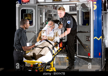 I paramedici la cura per il paziente anziano sulla barella in ambulanza a notte Foto Stock