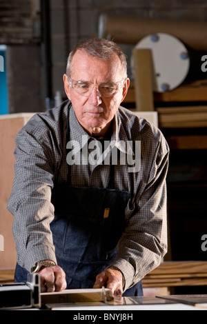 Senior uomo in macchine per la lavorazione del legno negozio utilizzando sega da tavolo Foto Stock