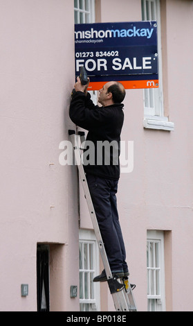 Un uomo attribuisce un per la vendita a bordo di una proprietà. Foto di James Boardman Foto Stock