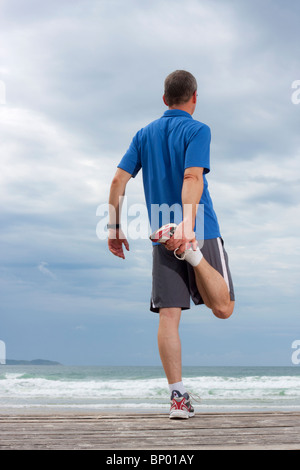 Runner facendo stretching esercita su di una spiaggia Foto Stock