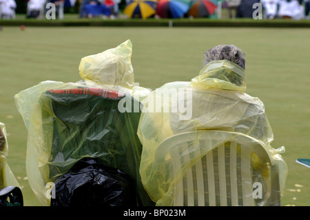 Persone che indossano macks plastica signore guardare partite di bocce Foto Stock