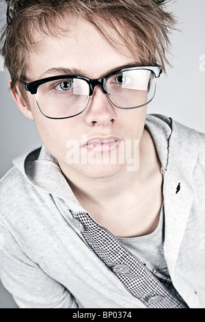 Colpo di geeky cercando adolescente contro uno sfondo grigio Foto Stock