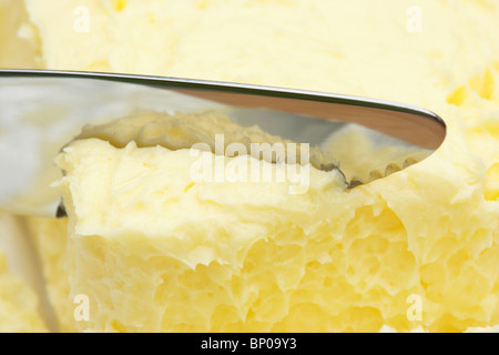 Il taglio della lama di una noce di burro fuori da un blocco di 250g morbido burro irlandese Foto Stock