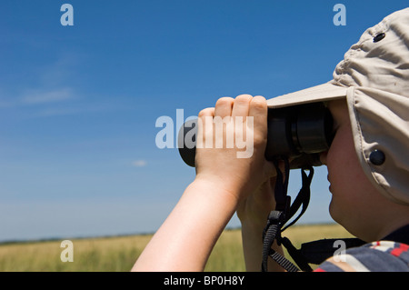 Kenia Masai Mara. Un giovane ragazzo su safari guarda fuori attraverso la savana con il suo binocolo (MR) Foto Stock