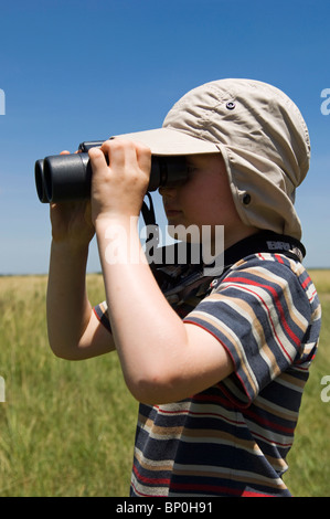 Kenia Masai Mara. Un giovane ragazzo su safari guarda fuori attraverso la savana con il suo binocolo (MR) Foto Stock