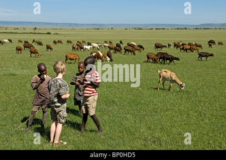 Kenia Masai Mara. Un giovane ragazzo su Safari Masai incontra i bambini tendono le loro greggi di capre e pecore fuori sulla pianura. Foto Stock