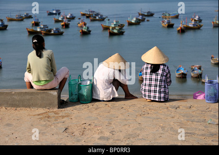 Le donne siedono, affacciato sul porto pieno di barche da pesca. Mui Ne, Vietnam Foto Stock