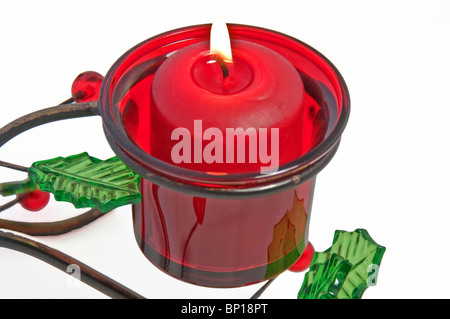 Questo rosso candela votiva è accesa e la masterizzazione in un titolare di Natale che è in metallo con vetro holly foglie e bacche, isolata. Foto Stock