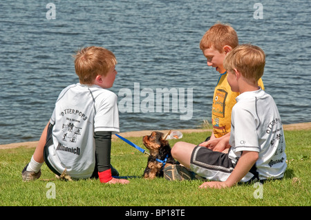 Questi tre ragazzi sono fuori a giocare sul prato vicino all'acqua con un molto piccolo Yorkshire Terrier cucciolo. Foto Stock