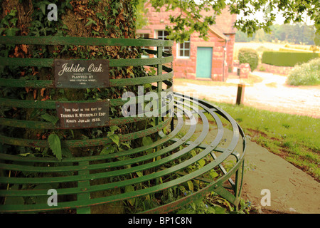 Questo sedile sotto la quercia giubilare rende un benvenuto luogo di riposo in Clive, Shropshire Foto Stock