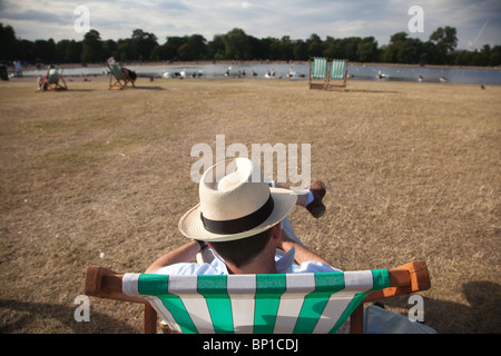 Un uomo che indossa un cappello di Panama si siede su un striped sedia a sdraio a Hyde Park, Londra. Foto:Jeff Gilbert Foto Stock