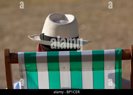 Un uomo che indossa un cappello di Panama si siede su un striped sedia a sdraio a Hyde Park, Londra. Foto:Jeff Gilbert Foto Stock