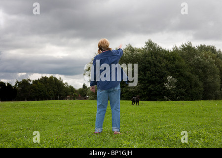 Una signora utilizza un flinger a lanciare una palla da tennis per il suo Labradoodle cane in una campagna parco con una tempesta imminente Foto Stock