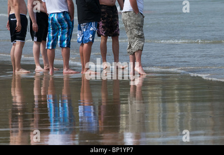 Un gruppo di turisti maschio permanente sulla spiaggia a Newquay in Cornovaglia. Foto Stock
