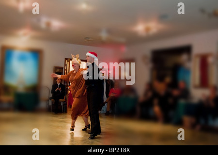 Senior Citizen lady con Rudolph costume indossando un luminoso naso rosso, balli in una sala da ballo con una rassegna di danza. Foto Stock