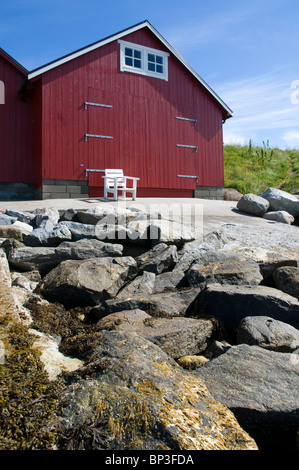 Rosso boathouse in legno sulla costa occidentale della Norvegia con sedia vuota Foto Stock