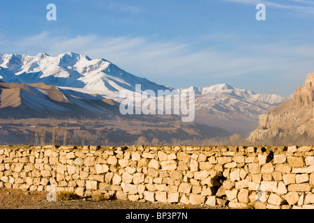 Afghanistan, Bamiyan. Recinzione in pietra con lo snow-capped Hindu Kush montagne sullo sfondo Foto Stock