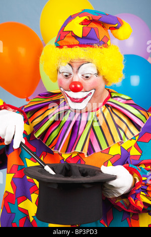 Compleanno clown esecuzione di un atto di magia con un tophat e bacchetta magica. Foto Stock