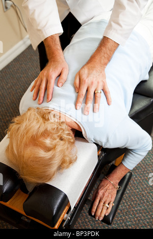 Primo piano di un chiropratico le mani come egli regola un paziente anziano nel suo ufficio. Foto Stock
