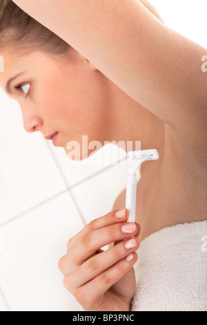 Giovane donna di rasatura delle ascelle di lei in bagno, concentrarsi sul rasoio Foto Stock