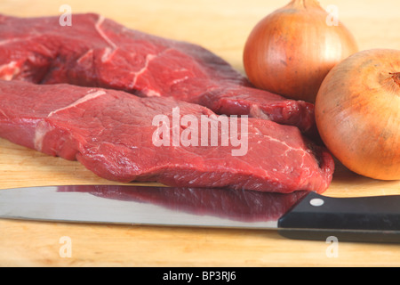 Due pezzi di materie bistecca, un Coltello per cuoco e un paio di cipolle, un buon punto di partenza per molti piatti diversi Foto Stock